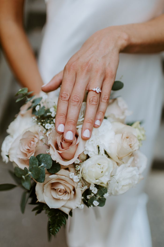 who-we-are Close-up of a bridal bouquet and manicured hand showcasing an elegant engagement ring.