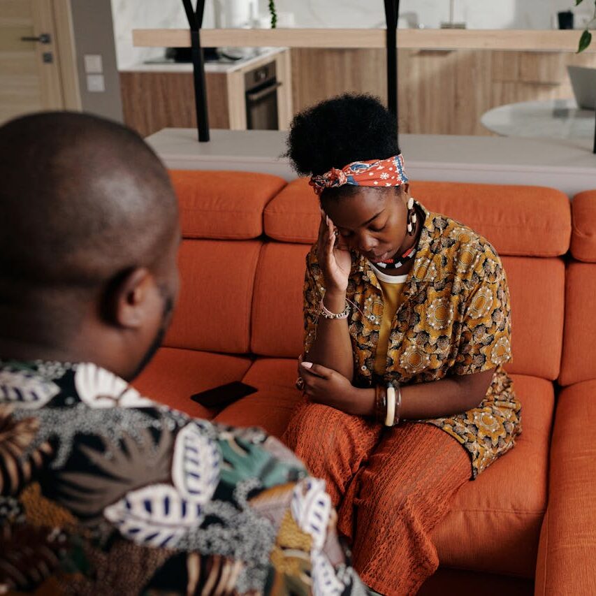 Emotional couple sitting on an orange sofa indoors, experiencing a heartfelt moment.